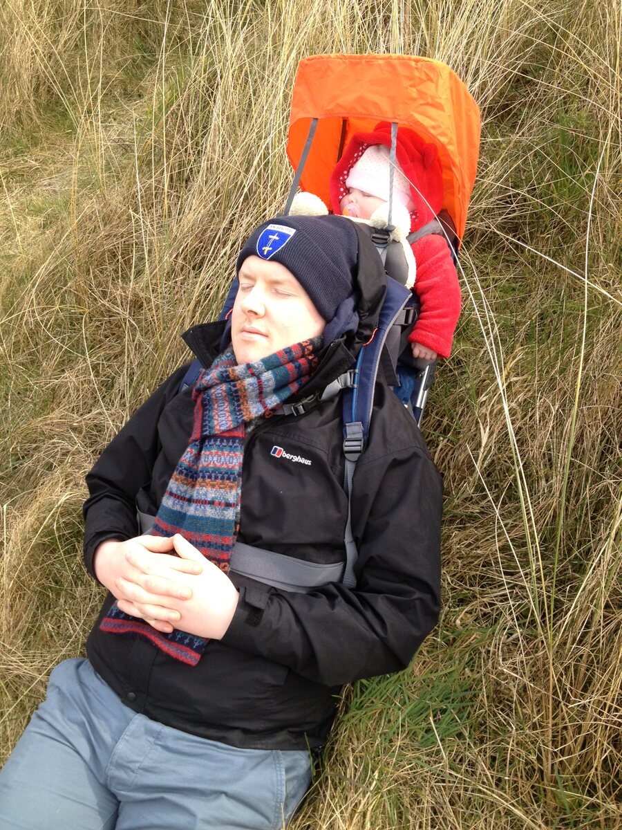 A parent resting outdoors with a child in a carrier.